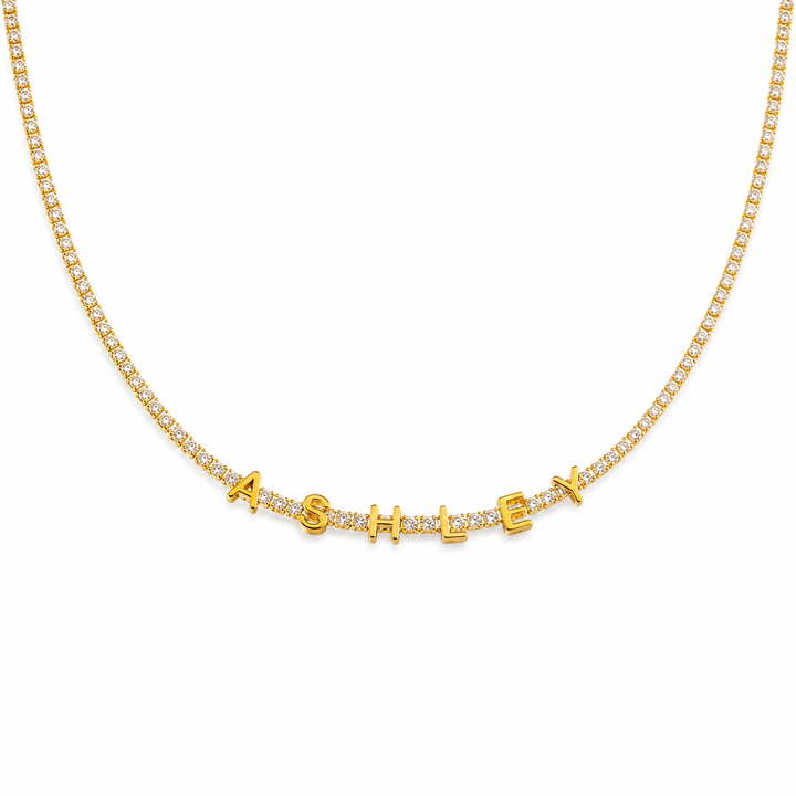 Gold tennis chain spelling ASHLEY in block letters, laid flat on white