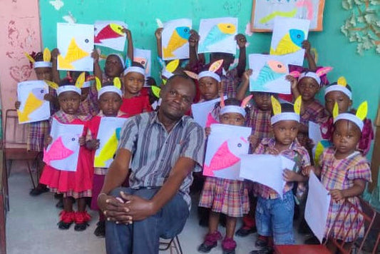 Students and their teacher in a Cité Soleil classroom holding up their paper artwork