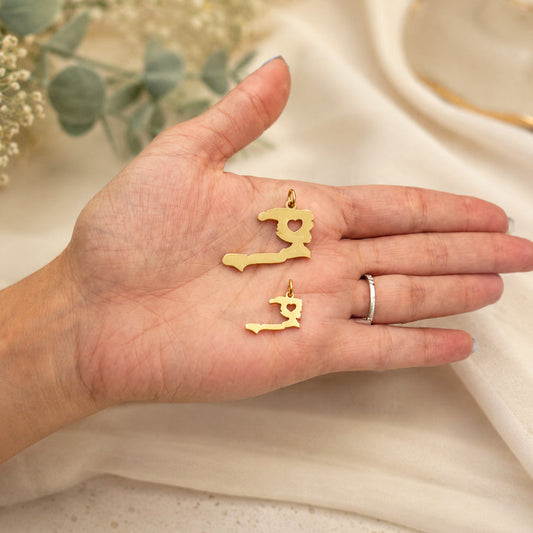Two sizes of the gold Ayiti Haiti-map charm held in an open palm