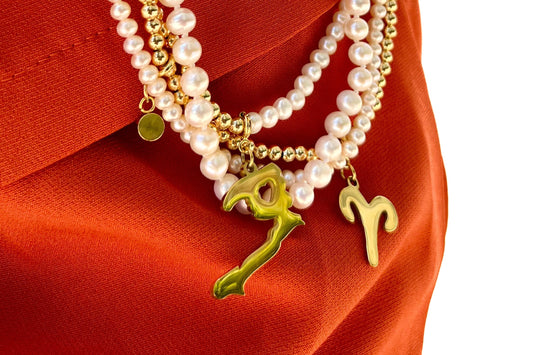 Layered pearl and gold bead necklaces with gold script initial charms on rust-orange silk