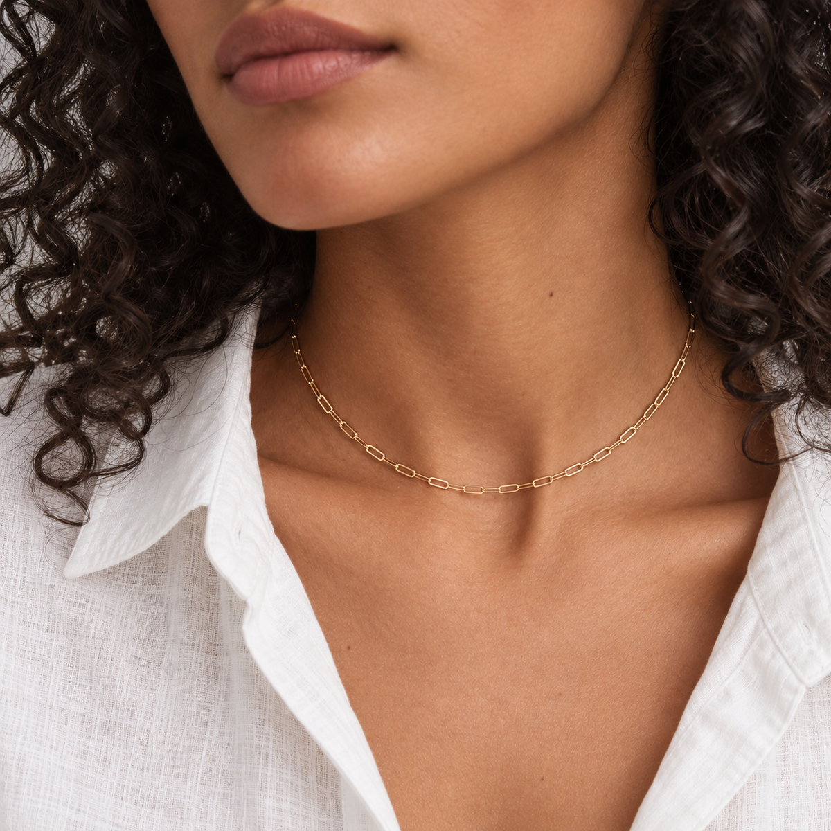 Paperclip choker worn at the base of the neck over an open white linen shirt