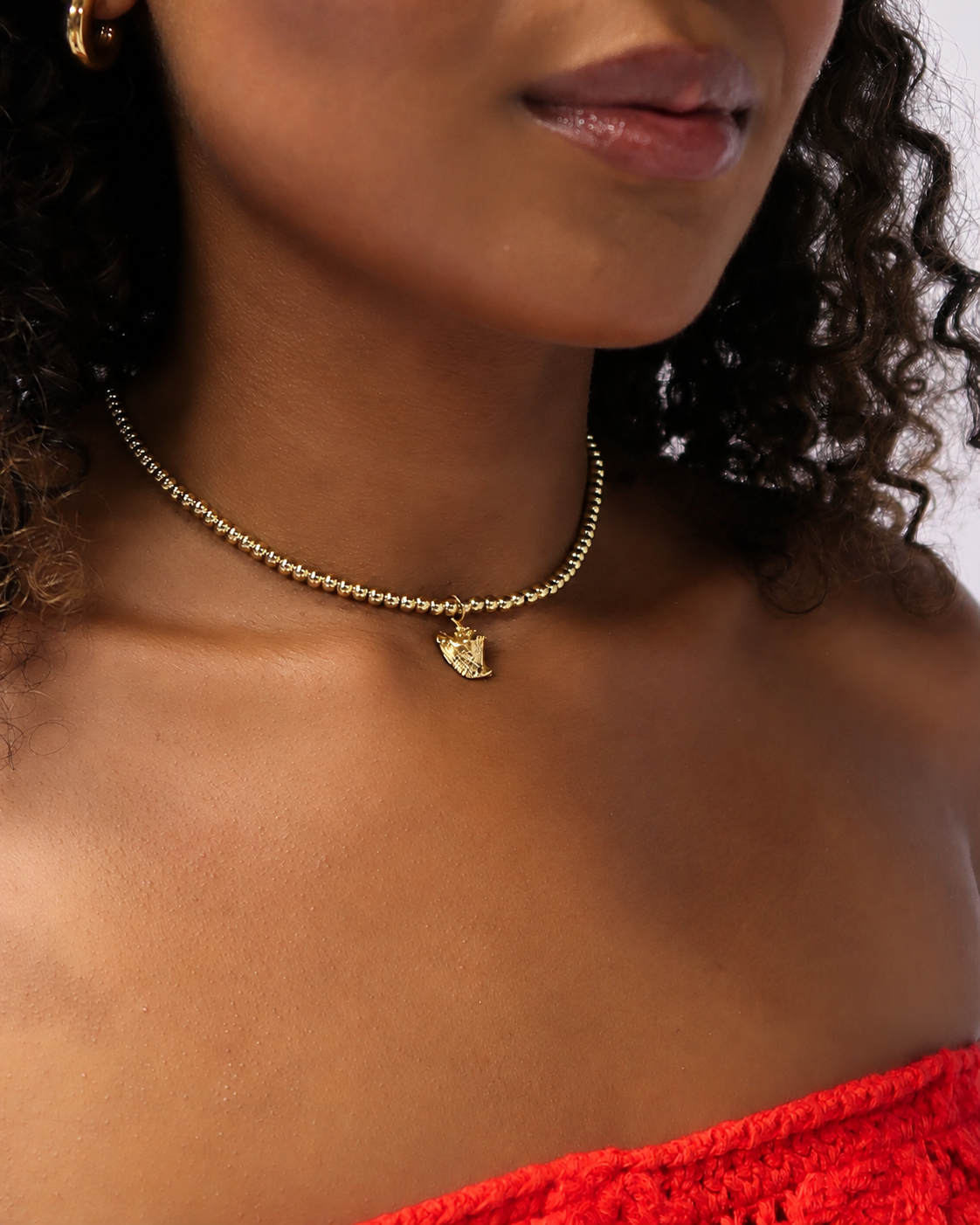 Lambi conch charm on a gold bead choker worn close at the neckline with red off-shoulder top