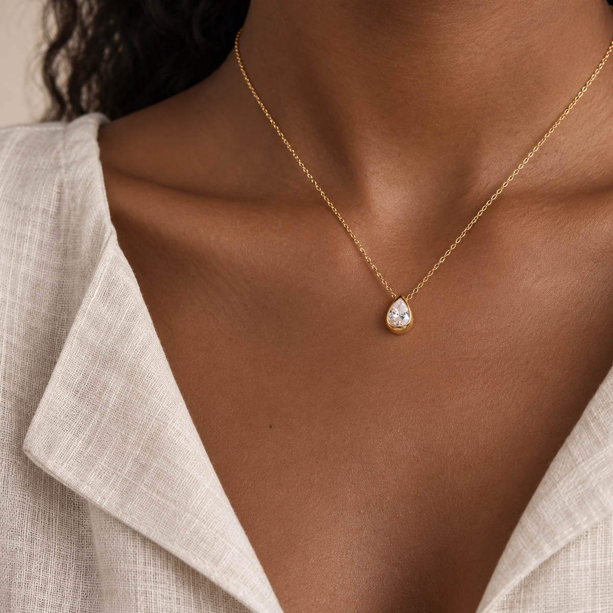 Gold bezel-set pear pendant worn at the collarbone on a fine chain