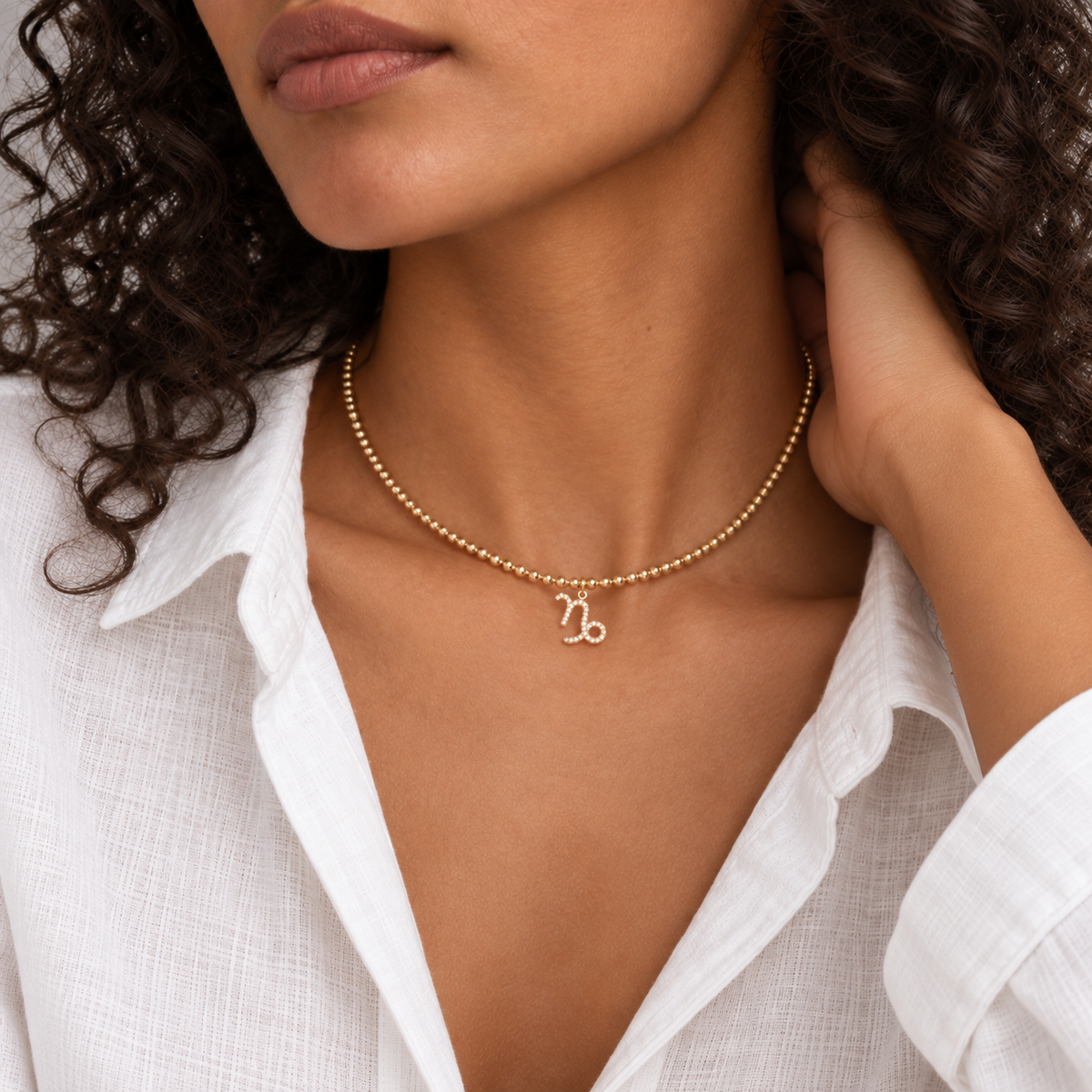 Gold bead zodiac choker worn at the collarbone with an open white linen shirt