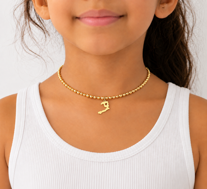 Ayiti map charm on a fine gold bead choker, worn at the neckline with a white tank