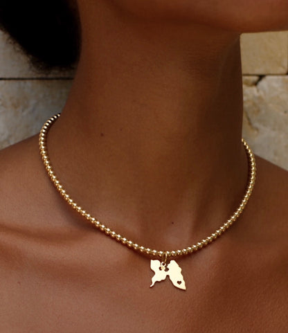 Guadeloupe map charm on a gold bead choker worn close at the neckline
