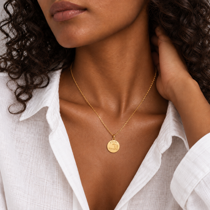Ayiti map coin pendant worn at the collarbone over an open white linen shirt