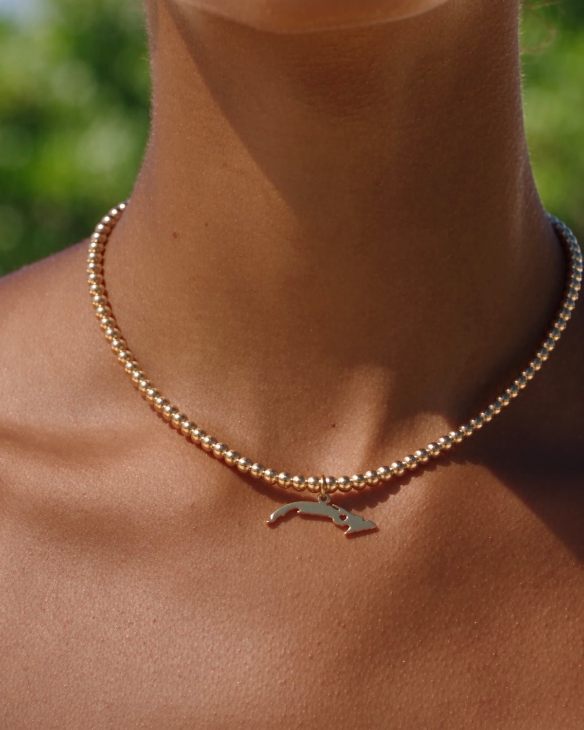Cuba charm on a gold bead choker worn close at the neckline outdoors
