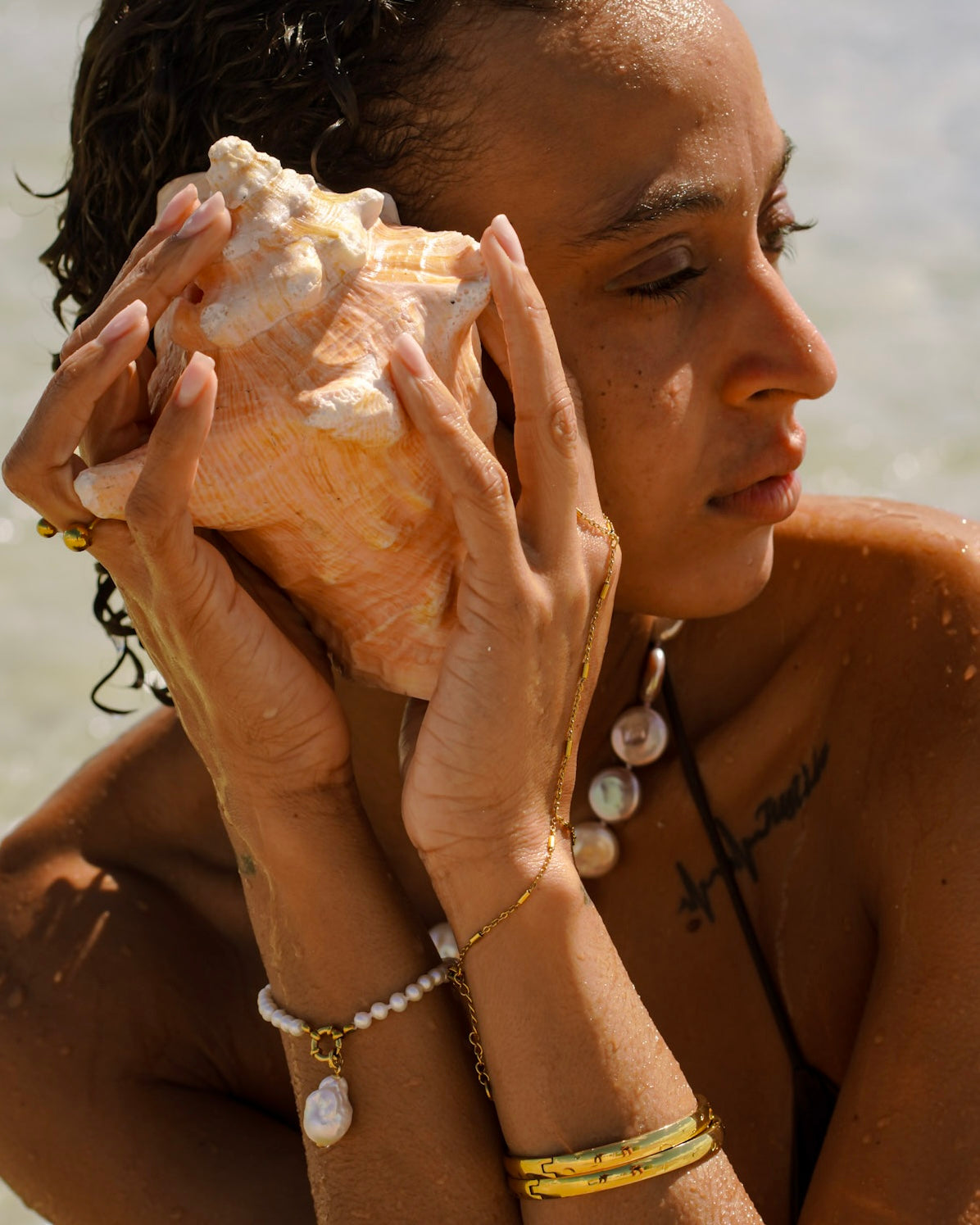 Gold and pearl jewelry worn by the sea while holding a conch shell